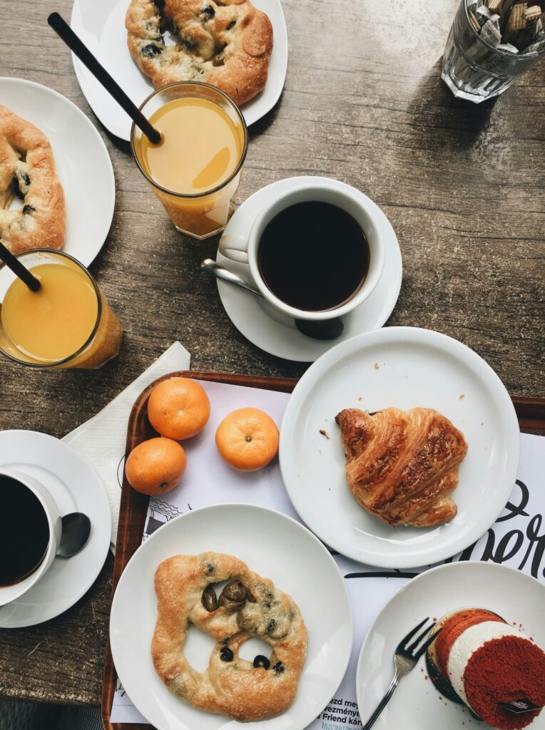 Frühstück mit Kaffee, Brezen und Obst auf einem Tisch.